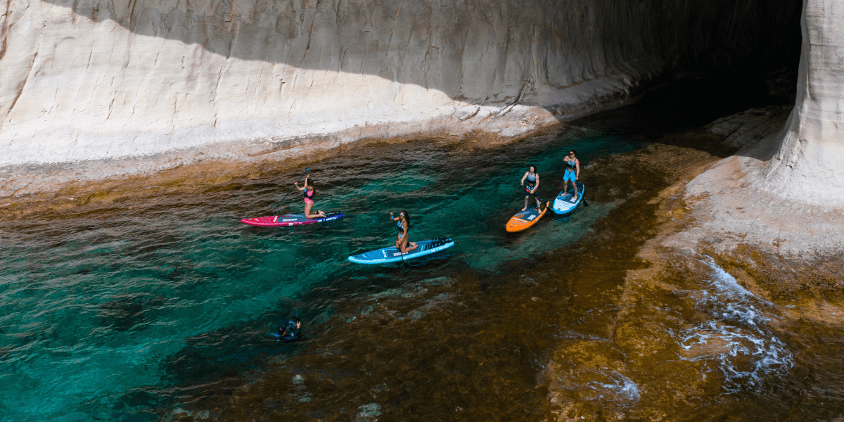 Four people paddleboarding next to some cliffs