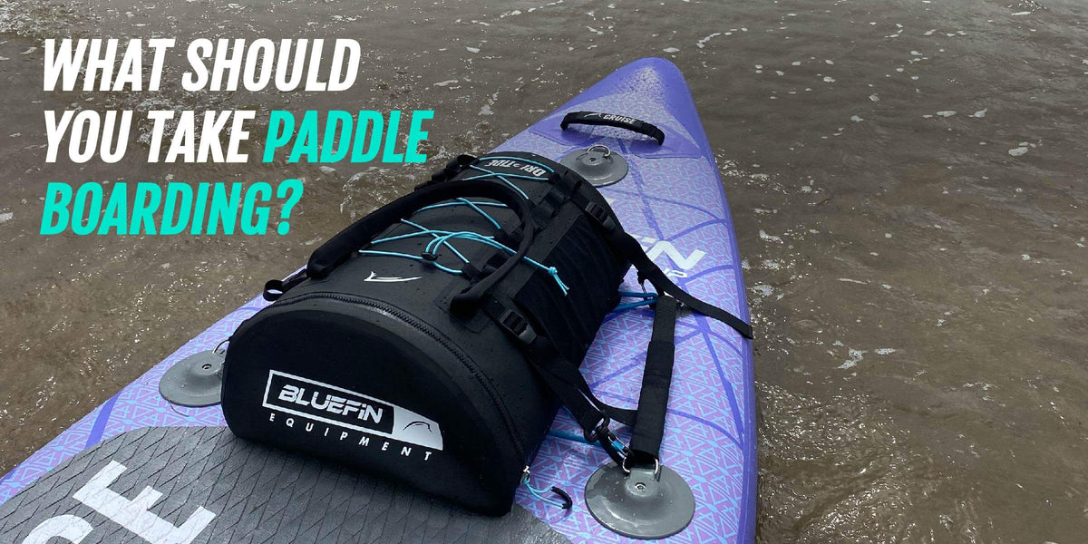 Tabla de paddle surf morada con bolsa de equipo negra en aguas poco profundas y texto sobre qué llevar