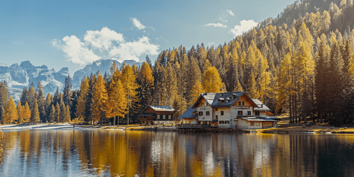 Lago alpino que refleja un bosque otoñal y un chalet, con montañas escarpadas al fondo
