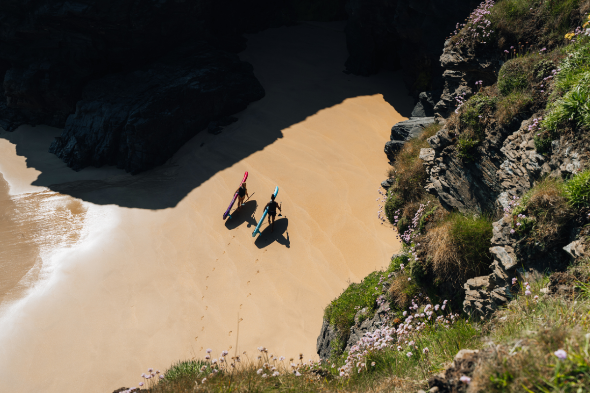 two people walking along a beach with their paddleboards