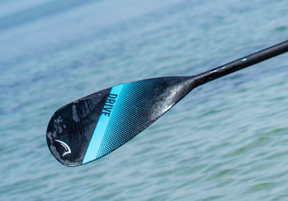 Close-up of a black paddle blade with blue stripe and 'DRIVE' text, above water surface.