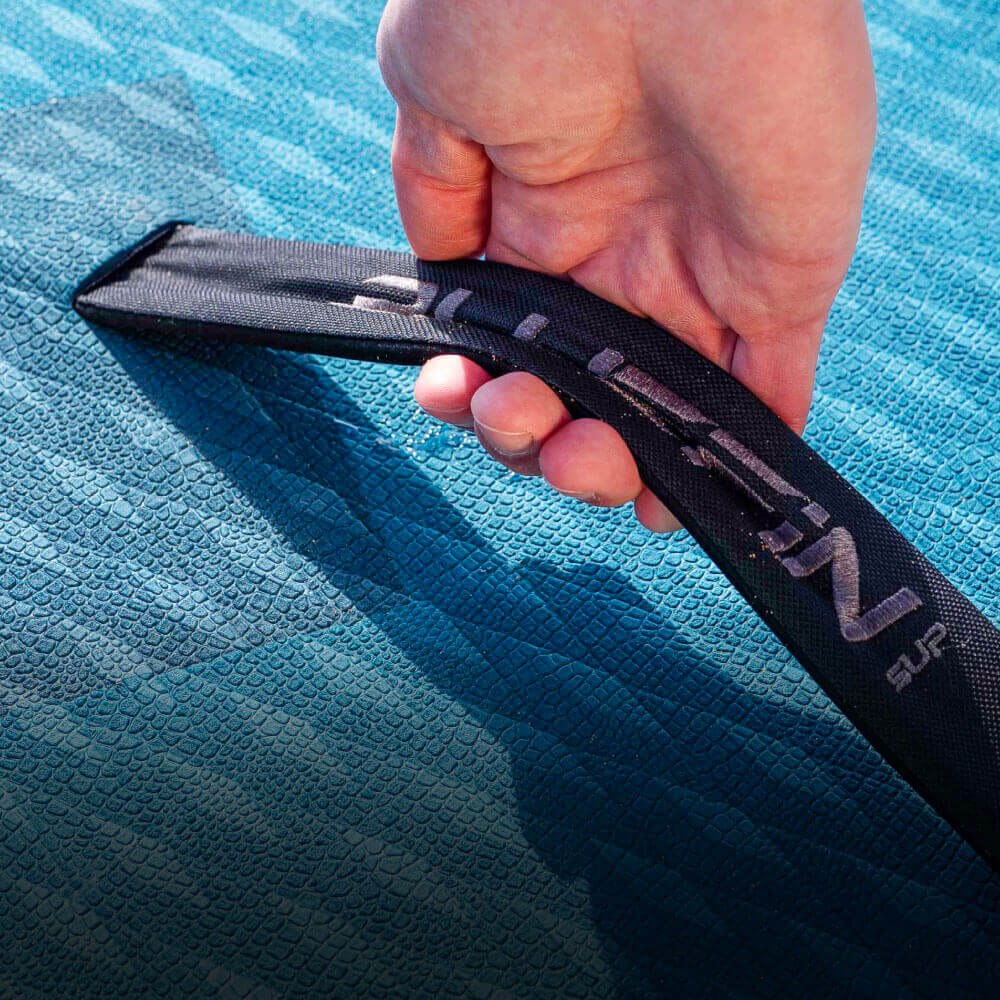 Hand holding a black strap labeled Bluefin SUP on a textured blue paddleboard surface
