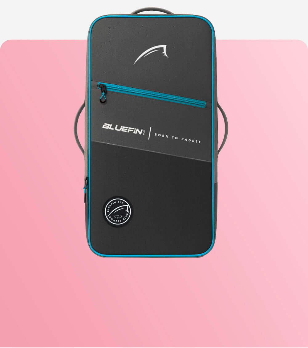 Black and teal paddleboard bag with logo, front zip pocket, and round patch on pink background