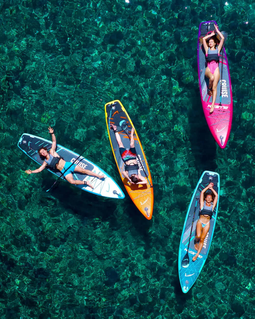 Cuatro paddleboarders relajándose en tablas coloridas en agua clara, disfrutando de un día soleado.