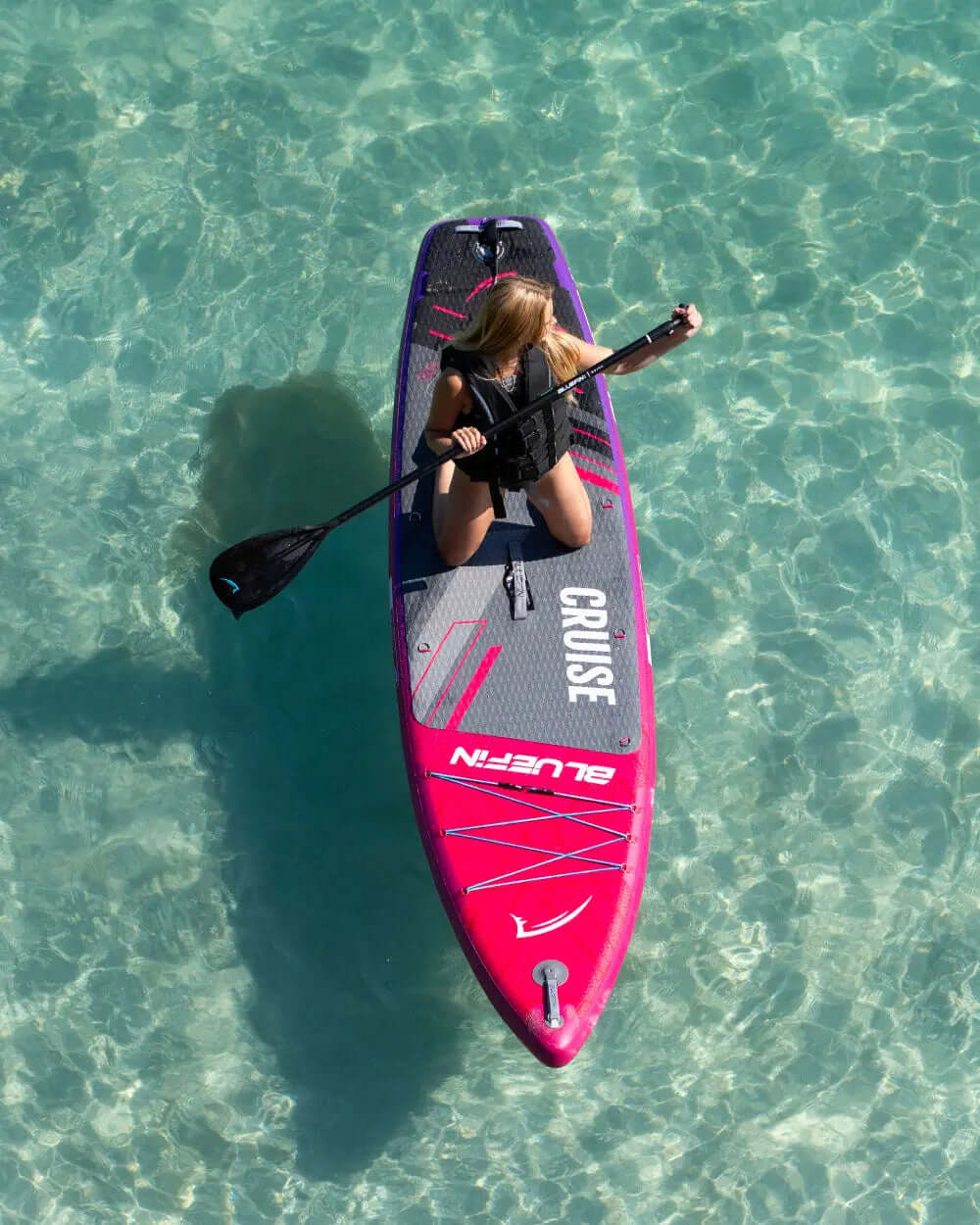 Paddleboard with pink and gray design, person paddling in clear water, wearing a life jacket