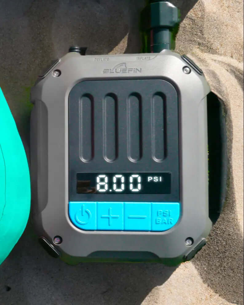Manómetro digital mostrando 8.00 PSI, con botones de inflar y desinflar, sobre una superficie arenosa.