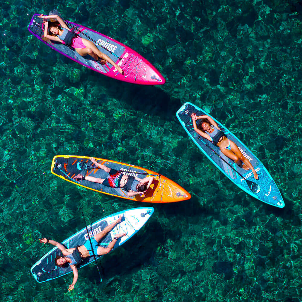 Four paddleboarders relaxing on colorful inflatable paddleboards in clear water.
