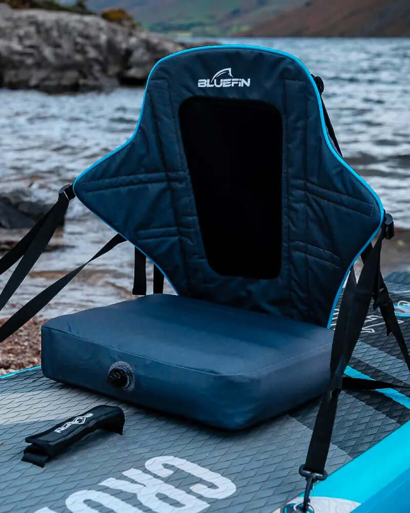 Bluefin paddleboard seat with backrest and cushion, adjustable straps, near water's edge.