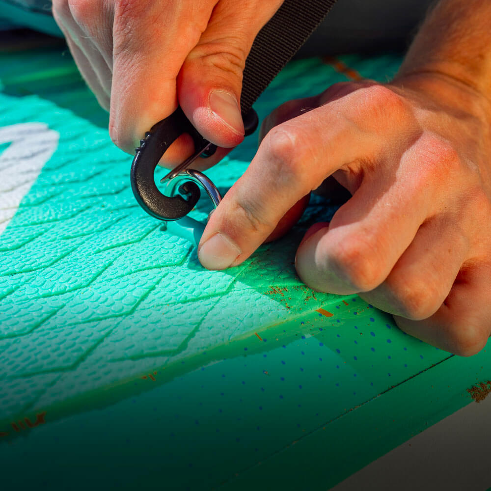 Close-up of hands attaching a strap to a textured green paddleboard surface