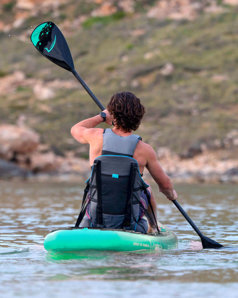 Person paddling a green inflatable paddleboard with a black paddle in calm water
