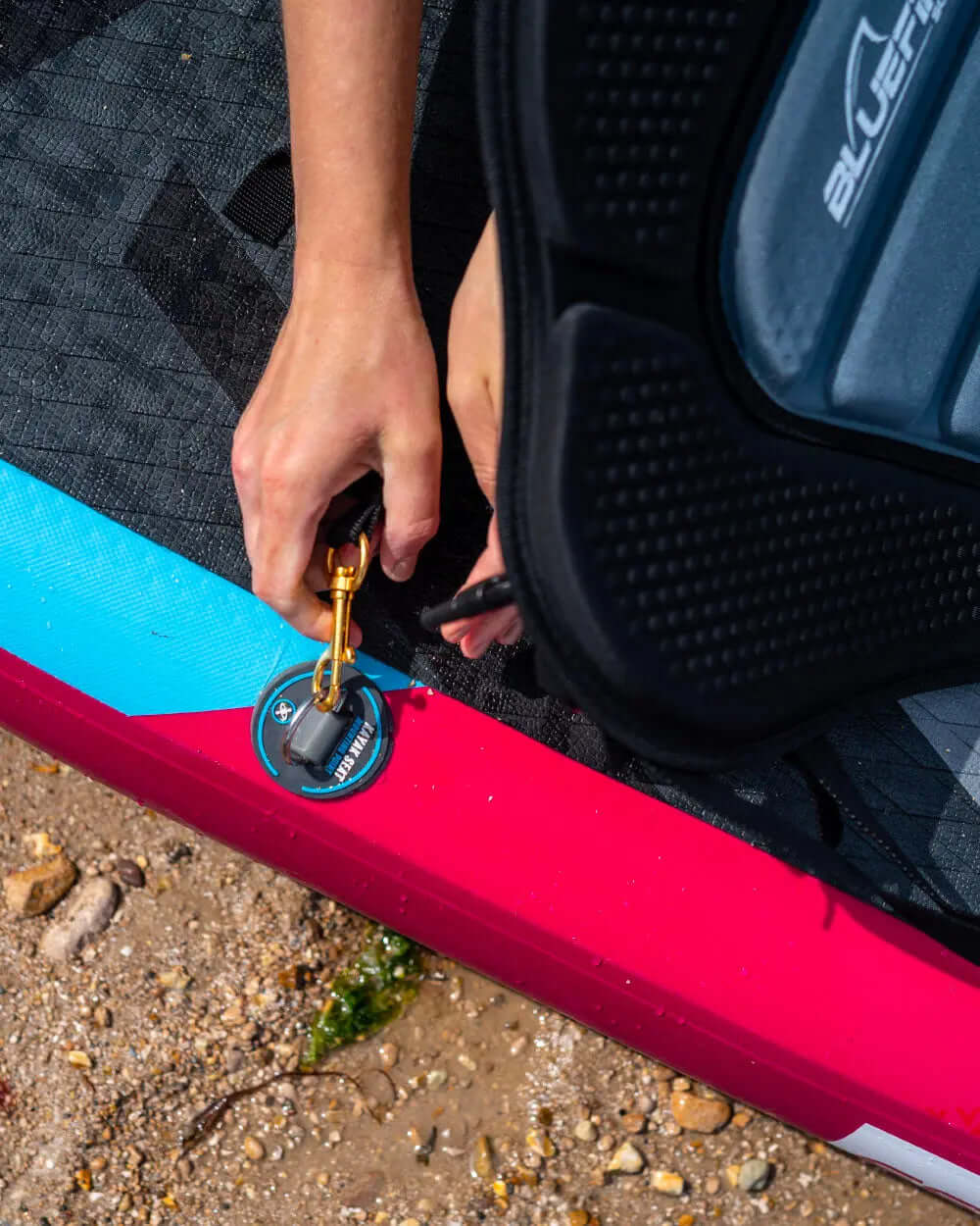 Hand attaching a safety leash to the inflation valve on a paddleboard's edge