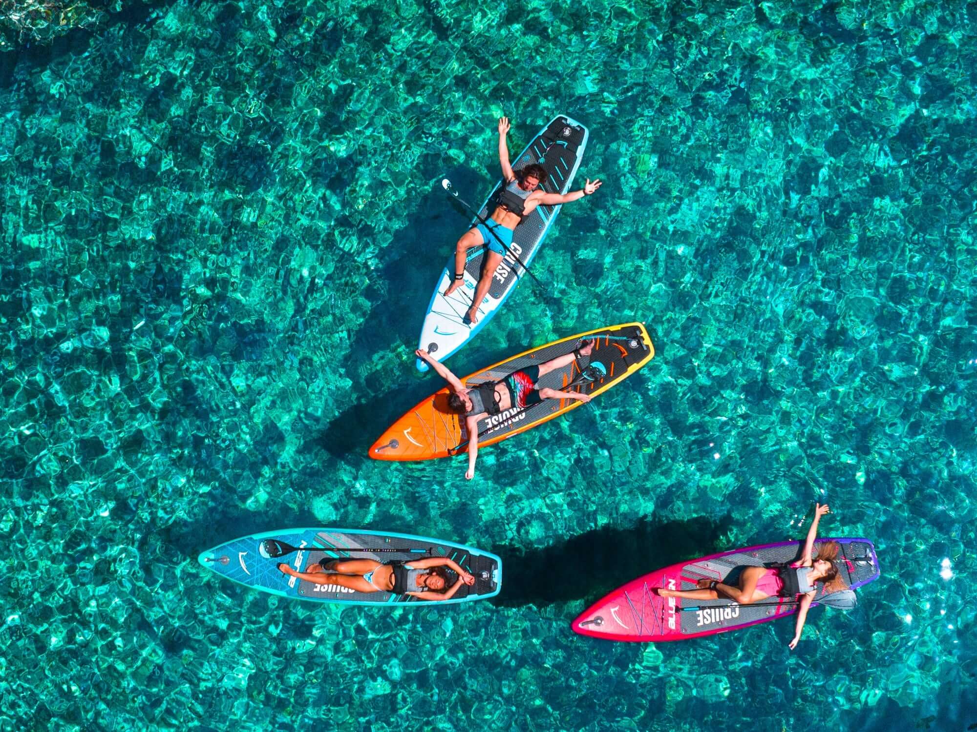 Cuatro practicantes de paddle surf relajándose sobre tablas coloridas en aguas turquesas claras