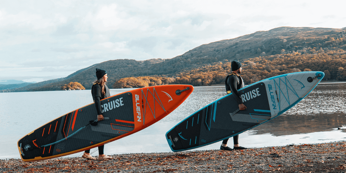 two people holding paddleboards infront of a lake