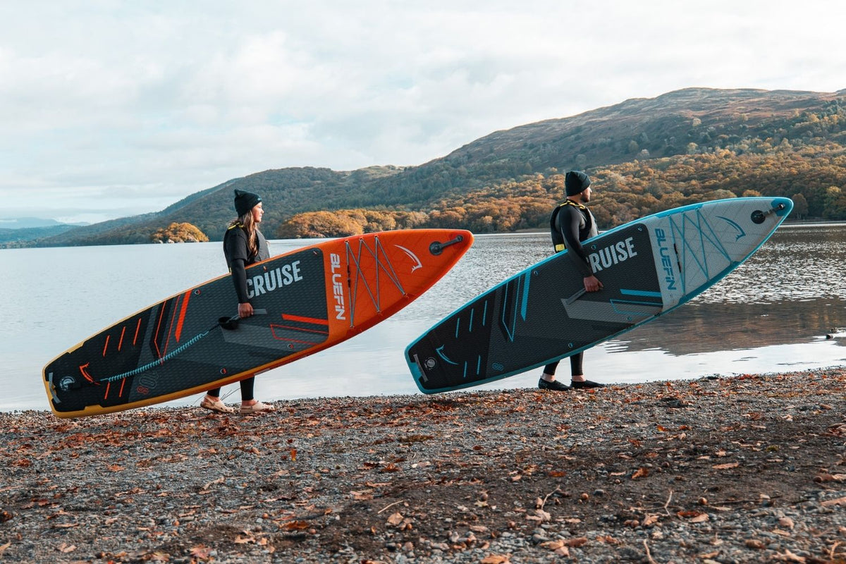 Dos personas sujetando tablas de paddle surf a la orilla del lago