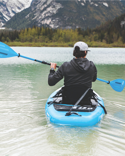 Person paddling a blue inflatable paddleboard on calm water with mountains in the background