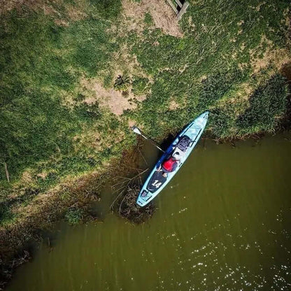 Aerial view of a blue kayak on a green riverbank with a person paddling and grass surrounding the water.