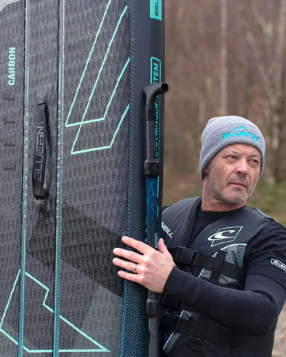 Man in a gray beanie holding a Bluefin inflatable paddleboard with textured surface and fin.