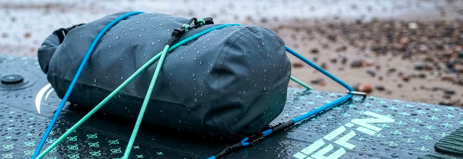 Waterproof bag secured with blue straps on a paddleboard, with raindrops visible on the surface.