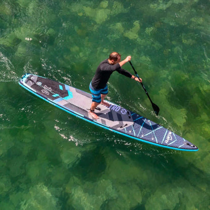 Hombre remando en una tabla de paddle inflable azul y negra sobre agua clara y verde