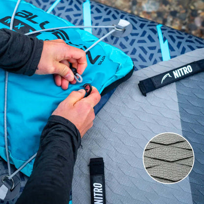 Manos asegurando una bolsa de tabla de paddle inflable azul con una almohadilla de cubierta texturizada gris y correa NITRO.