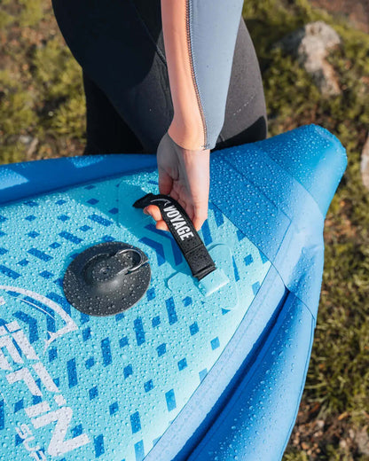 Person holding a blue inflatable paddleboard with a textured deck and water droplets on it
