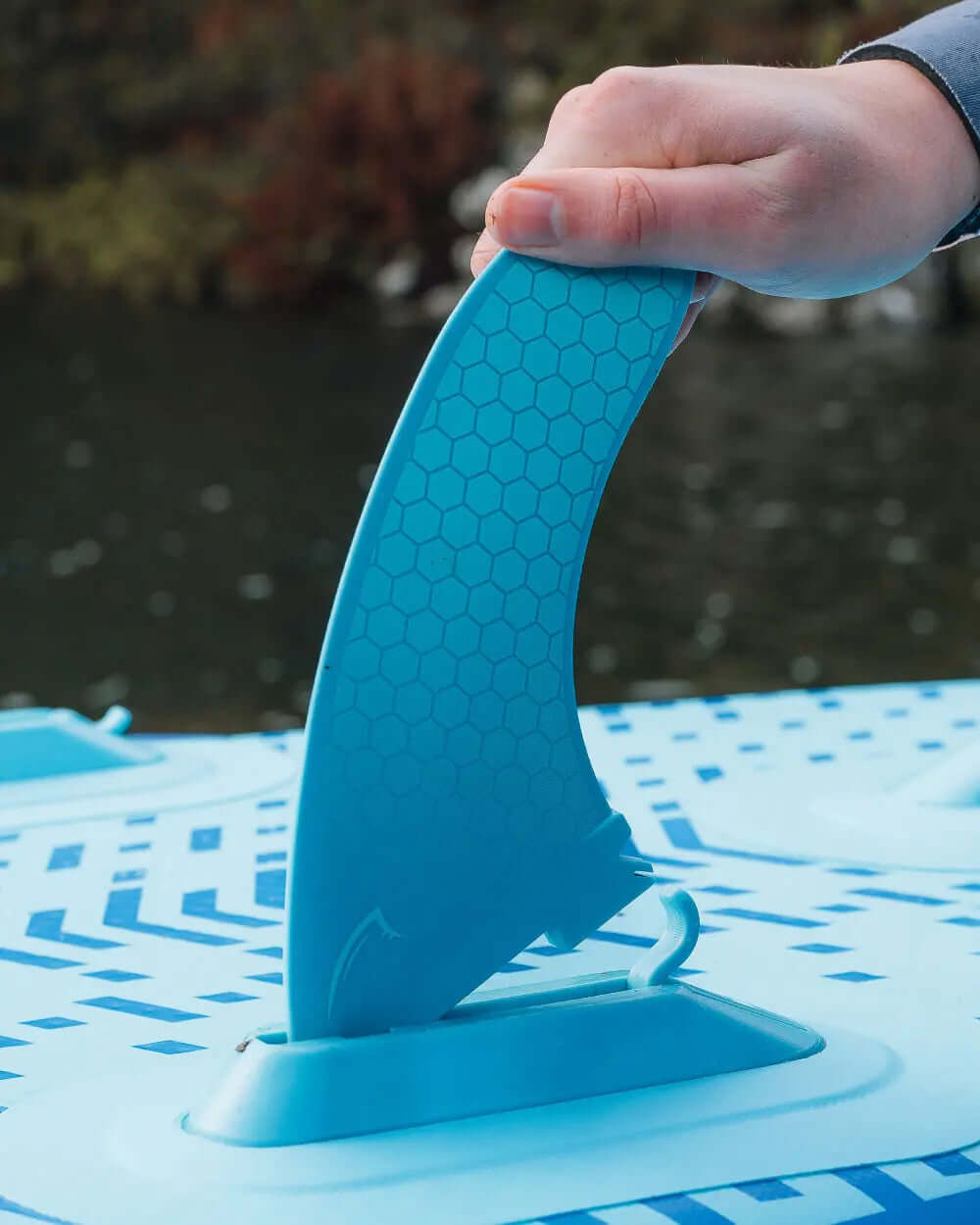 Hand holding a blue fin while attaching it to an inflatable paddleboard on water